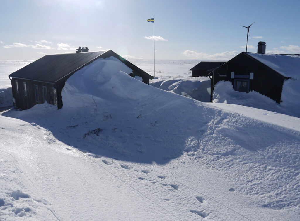 Schneeakkumulation im Windschatten einer Hütte in der kleinen Hüttensiedlung Rörsjöstugorna auf dem Hochplateau des Fulufjells am 10.03.2014